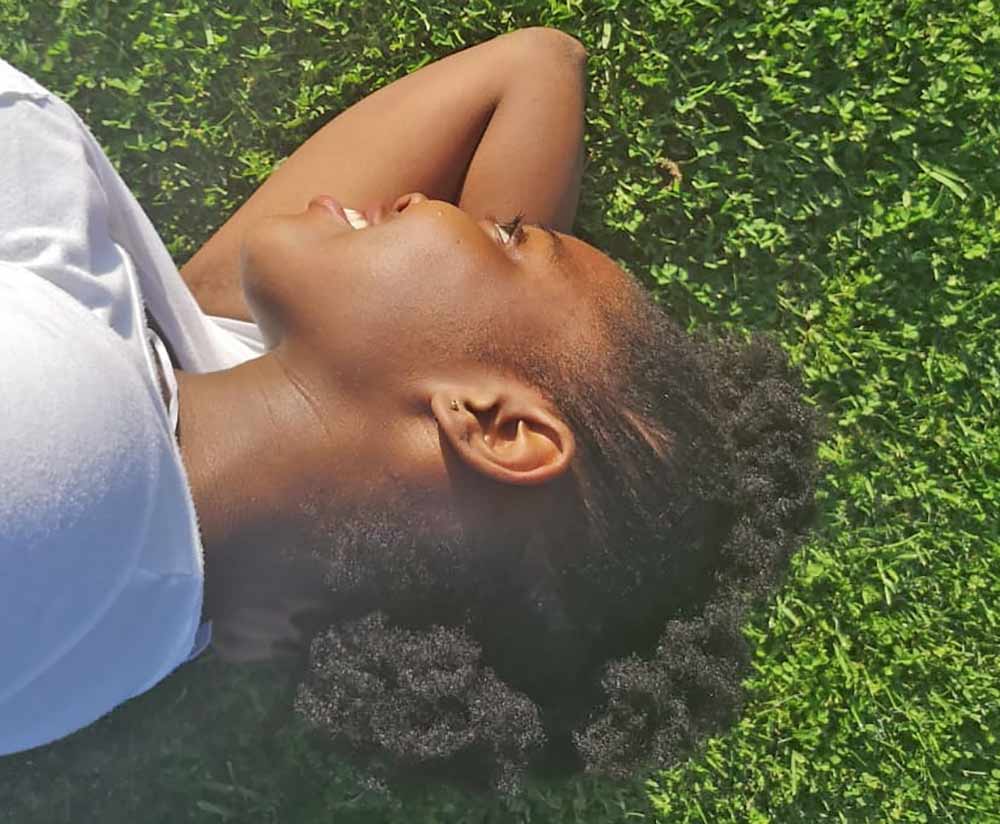 Picture showing an afro naturals lady lying on cut grass outside showing off hair which is treated afro hair done at home