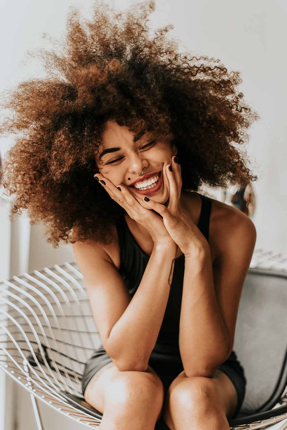 An African American woman laughing on a coach with natural 3C hair type