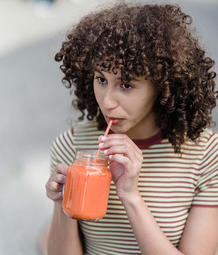 Girl with curly hair drinking beet and carrot smoothie for hair growth