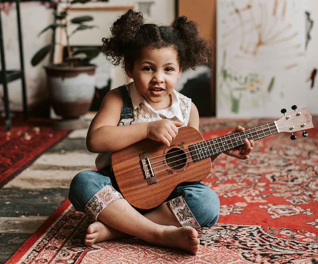 Little girl in pig tails sitting crosslegged on the floor with a guitar