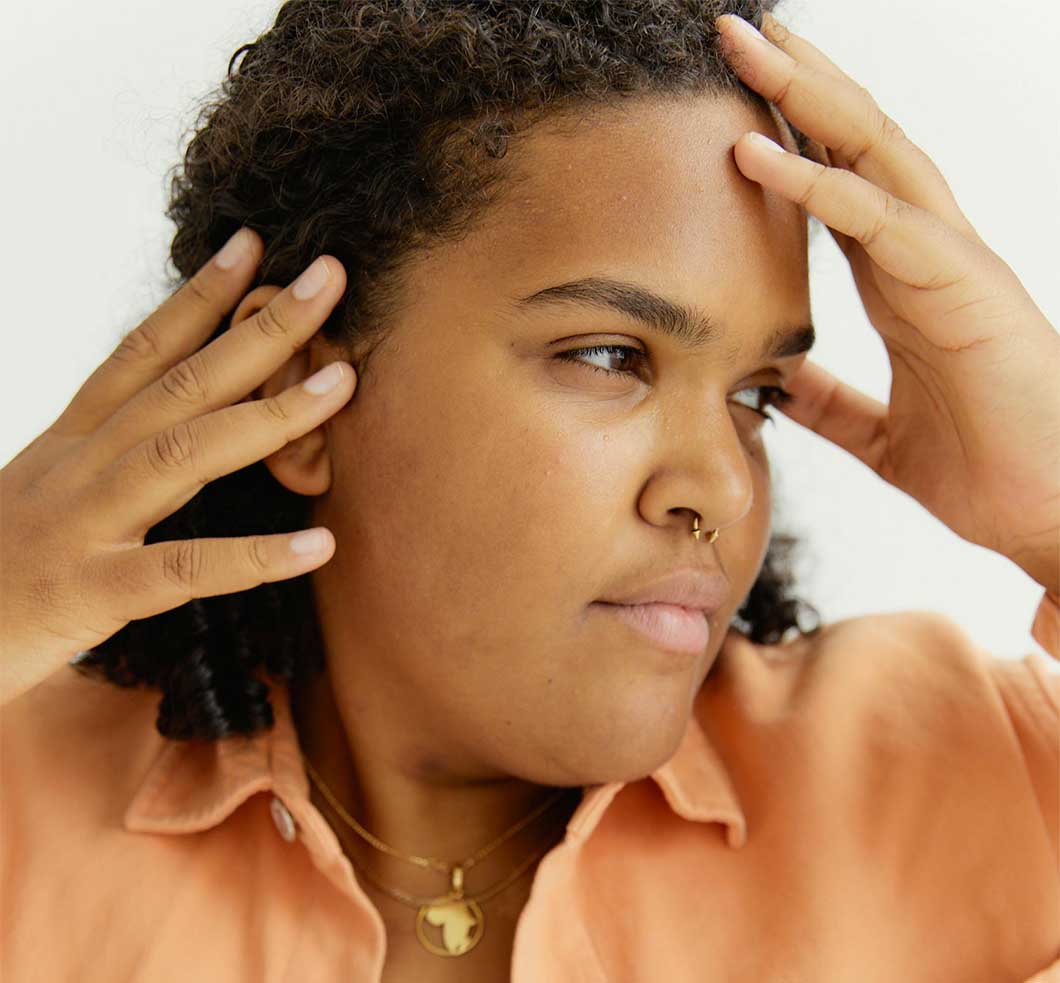 Woman with natural hair and sensitive scalp holding her head between her hands.